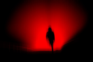 A dark, horror concept. Of a blurred hooded figure silhouetted against lights at night. With a black, red moody edit.