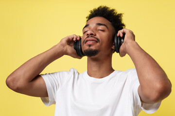 Fototapeta na wymiar Attractive African American man with headphones listen to music. Isolated over yellow gold background.