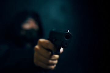 Man in hood threatens with firearm. Masked robber with gun. Weapon in person's hands. Murderer or armed thief. Criminal with pistol.