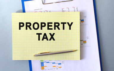 PROPERTY TAX text written on notepad with pencil. Notepad on a folder with diagrams.