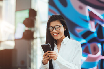 A young beautiful Asian woman is using an application in her phone to send a text message or browse e-commerce offers while in a shopping centre