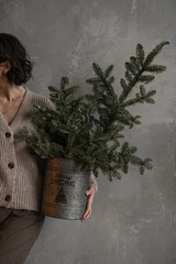 Young pretty woman hold in hands bucket with Christmas fir branches. Minimal fashion festive...