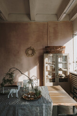 Elegant aesthetic home living or dinning room interior design with dinner table, linen table cloth, fir branch bouquet, Christmas wreath, neutral dusty pink walls. Sunlight shadows on the wall