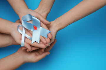 People holding light blue ribbons with paper blood drop on color background, top view and space for text. Diabetes awareness