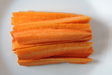 Orange carrot sticks on a white plate, white background