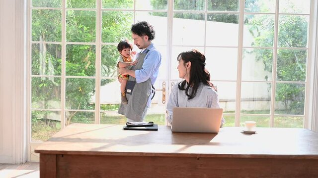 ママのパソコンリモートワークを支える素晴らしく気の利くパパと抱っこされる赤ちゃんの動画