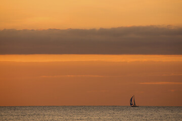 A small sailing boat on the open sea at sunset
