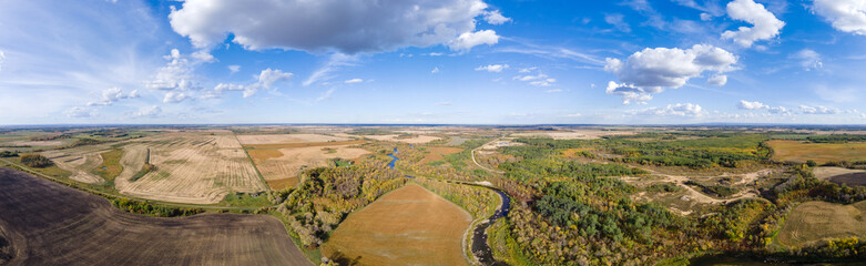 Fototapeta na wymiar Aerial panorama of a vast prairie in autumn colors with white clouds in a blue sky. A river cuts through the scene. 