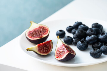 Figs and blueberries on white plate, close up, selective focus. Modern minimalist still life.