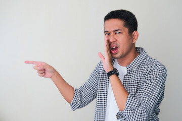Adult Asian man whispering gossip and pointing finger to someone