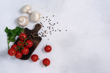 Red, ripe cherry tomatoes, champignons, and parsley are lying on a bright table. Top view, space for text
