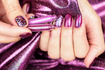 Festive purple manicure with sparkles and shimmer. Beautiful female hand with shiny purple manicure on a purple background. Christmas manicure.