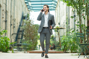 A young successful businessman is working outdoor using smartphone. Man in a casual wear. Business, freelance and remote work.