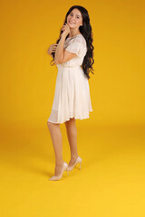 young beautiful brunette girl with long hair in white dress yellow background