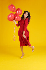 a young beautiful beautiful long-haired brunette girl in a red dress holds red balloons in her hands yellow background