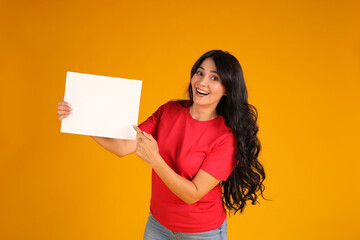 Naklejka na ściany i meble beautiful happy brunette girl with long hair in a red T-shirt holding a white sheet of paper yellow background