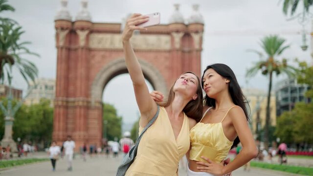 Smiling mixed-race females taking selfie or shooting blog while having fun outdoors in summertime
