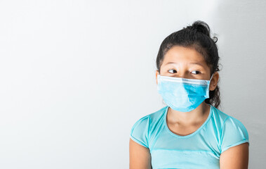 Thoughtful brunette girl while looking to the left side very bored, with blue blouse and surgical mask (8-year-old Latina) pandemic, quarantine, covid-19. medical concept. space for advertising text