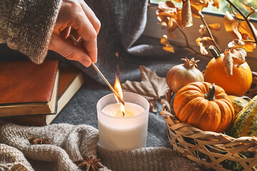 Hand with burning match lighting a candle on the windowsill with cozy autumn still life with...