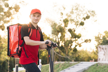 Young student works in a delivery service, with a red backpack and baseball cap, rides an electric...
