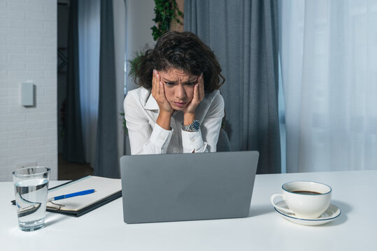 Young successful business woman sitting in an office and works on a laptop unable to work due to loud noise coming from the upstairs office where renovations are underway and workers are making noise