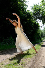 junge schöne Frau tanzt im Sommerlicht auf Waldweg