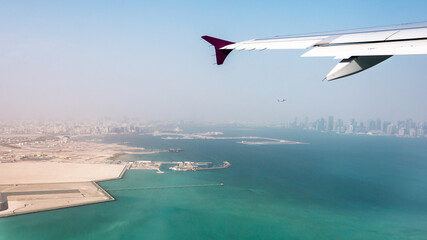 View of the city of Doha, Qatar from the airplane porthole. Plane flies over the skyscrapers. Travel concept.