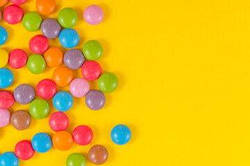 Colorful background of multicolored candy dragees. Round scattered sweets on a yellow bright background.