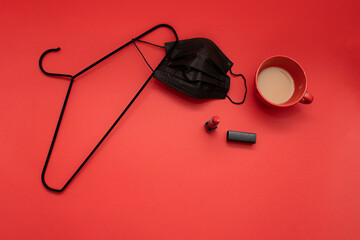 Black coronavirus medical mask hanging on the vibrant red background with red lipstick and coffee cup. Fashionable and creative mask on hanger for Halloween. Ready for the day.