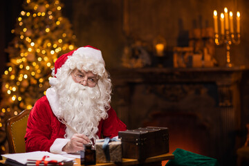 Workplace of Santa Claus. Cheerful Santa is writing the letter while sitting at the table....
