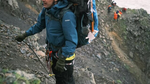 The climber climbs up the mountain with a backpack with equipment, fastened with a carabiner with a belay to the rope. A man climbs up to the top of the mountain