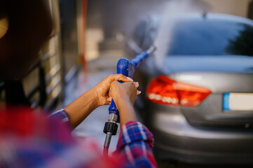 Woman using high pressure water gun, car wash
