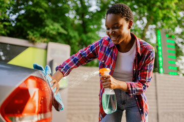 Woman using window cleaner spray, hand car wash