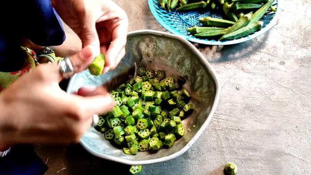 A closeup of a person cutting raw okras in slices into a bowl shot in 4K