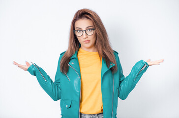 Clueless young woman against white background being in confusion with stretched arms opened palms, wearing green leather jacket, isolated on white background