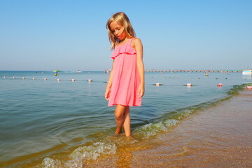Anapa, Russia, August 29, 2021. A 7-year-old girl in a pink dress walks along the sea. Blond hair...