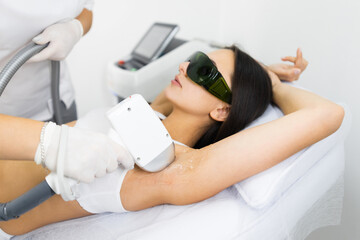 Obraz na płótnie Canvas Woman in white underwear doing laser hair removal on armpits in epilation salon