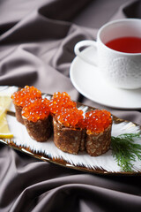 Red caviar pancakes and cup of tea on the satin cloth. Vertical composition.