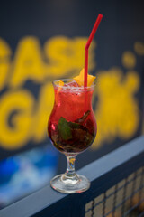 close up of a red cocktail on a blue fence with letters in the background