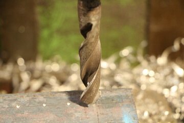 A drill for metal makes holes in a steel part on an industrial drilling machine.