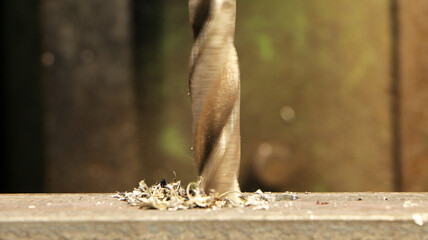 A drill for metal makes holes in a steel part on an industrial drilling machine.