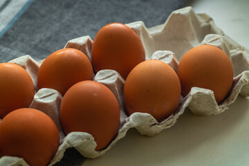 Cardboard box with brown chicken eggs on a gray napkin.