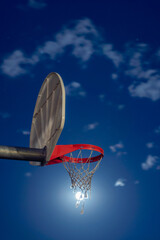 A closeup creative sports background photograph of a basketball hoop in a park at night with the moon as the ball going through a torn net.