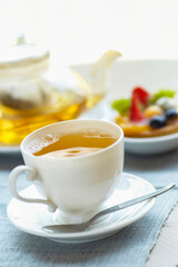 A cup of herbal tea with teapot and tart dessert on blue linen tablecloth. selective focus .