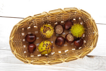 Several peeled and unpeeled chestnuts in a basket on a wooden table, close-up, top view.