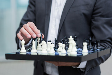 Close-up photo of a successful businessman holding a chessboard and making a move