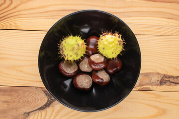 Several peeled and unpeeled chestnuts in a ceramic bowl on a wooden table, close-up, top view.