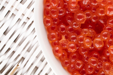 Weakly salted red caviar of chum salmon in white ceramic dishes on a mat made of vine, close-up, top view.
