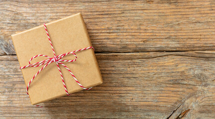 Christmas gift box on wooden background. Red white striped string tied on brown kraft present.