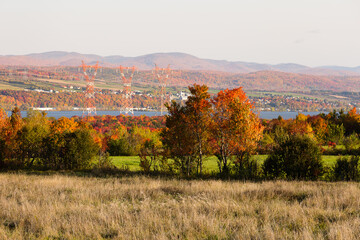 Colourful Fall foliage with power line towers and the St. Lawrence river in soft focus background,...